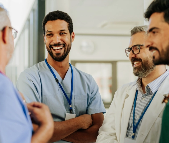 Five men in scrubs and badges smiling and talking to doctors and nurses