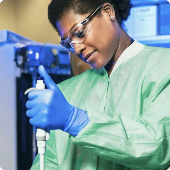 Woman in lab coat, gloves, and safety goggles using pipet