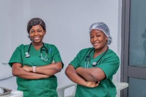 Two nurses wearing green scrubs, with their arms crossed smiling at the camera