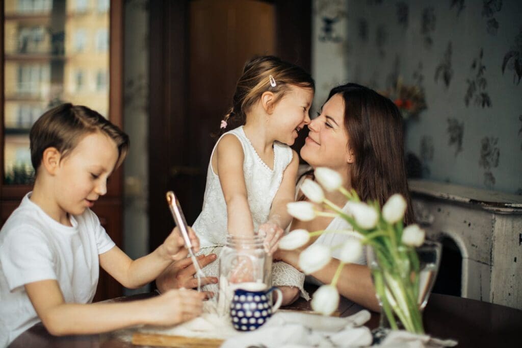 woman at a table with a boy and a girl, rubbing noses lovingly with the little girl