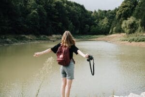woman with a backpack looking out at a lake with a camera in her hand