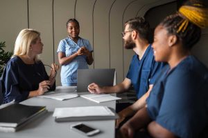 nurse standing in front of a conference table speaking to 3 other nurse administrators